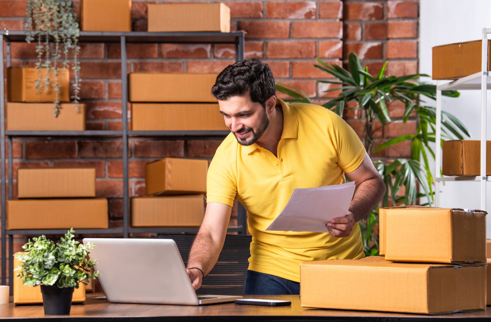 Online store owner checking orders on a laptop surrounded by parcels